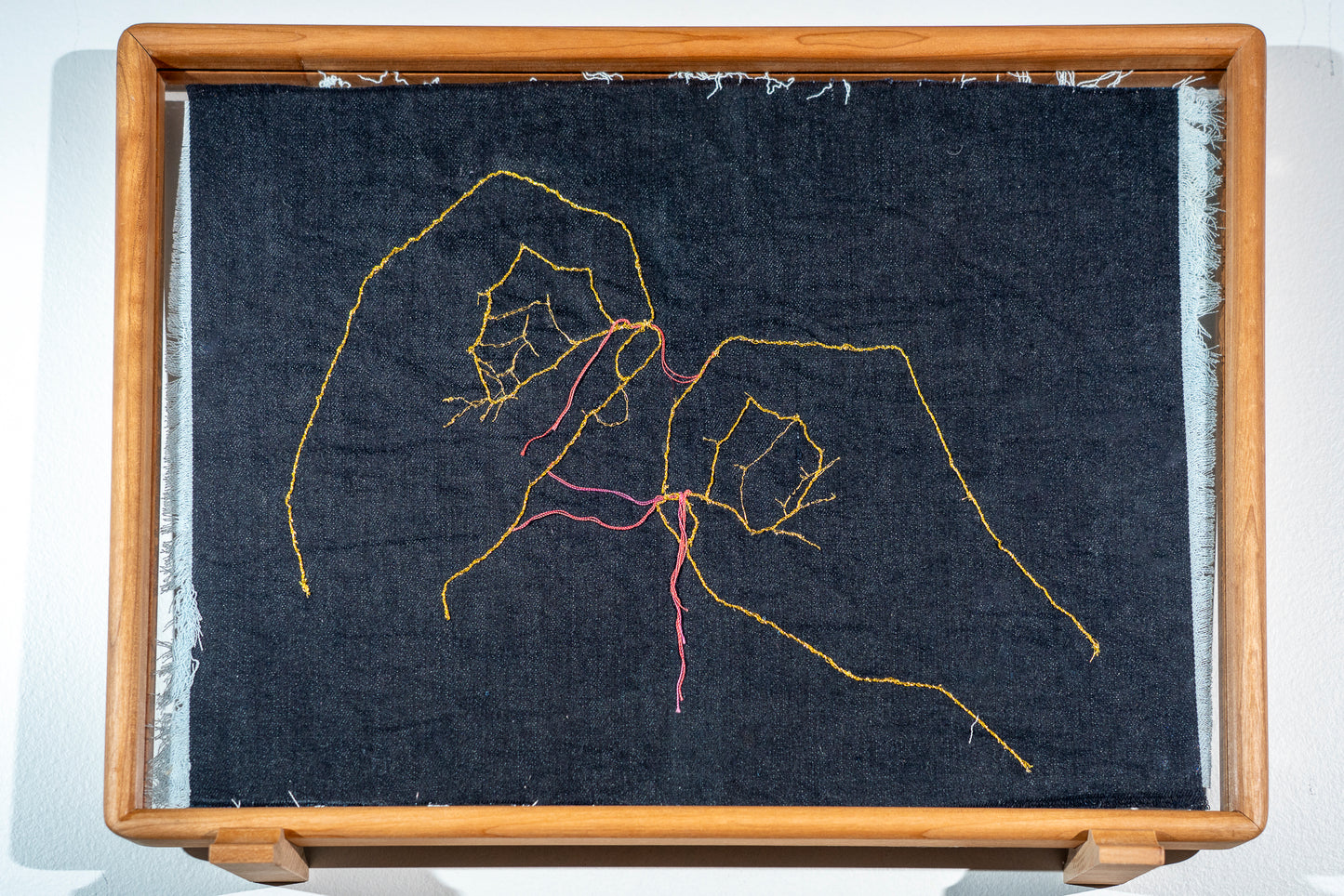 It is a double sided piece of denim with frayed edges, on each side is a pair of hands but on the dark side they are picking each other apart and on the light side they are sewing each other together with an actual needle embroidered into the piece. The hands are in gold thread but the threads being picked out are in shades of red.