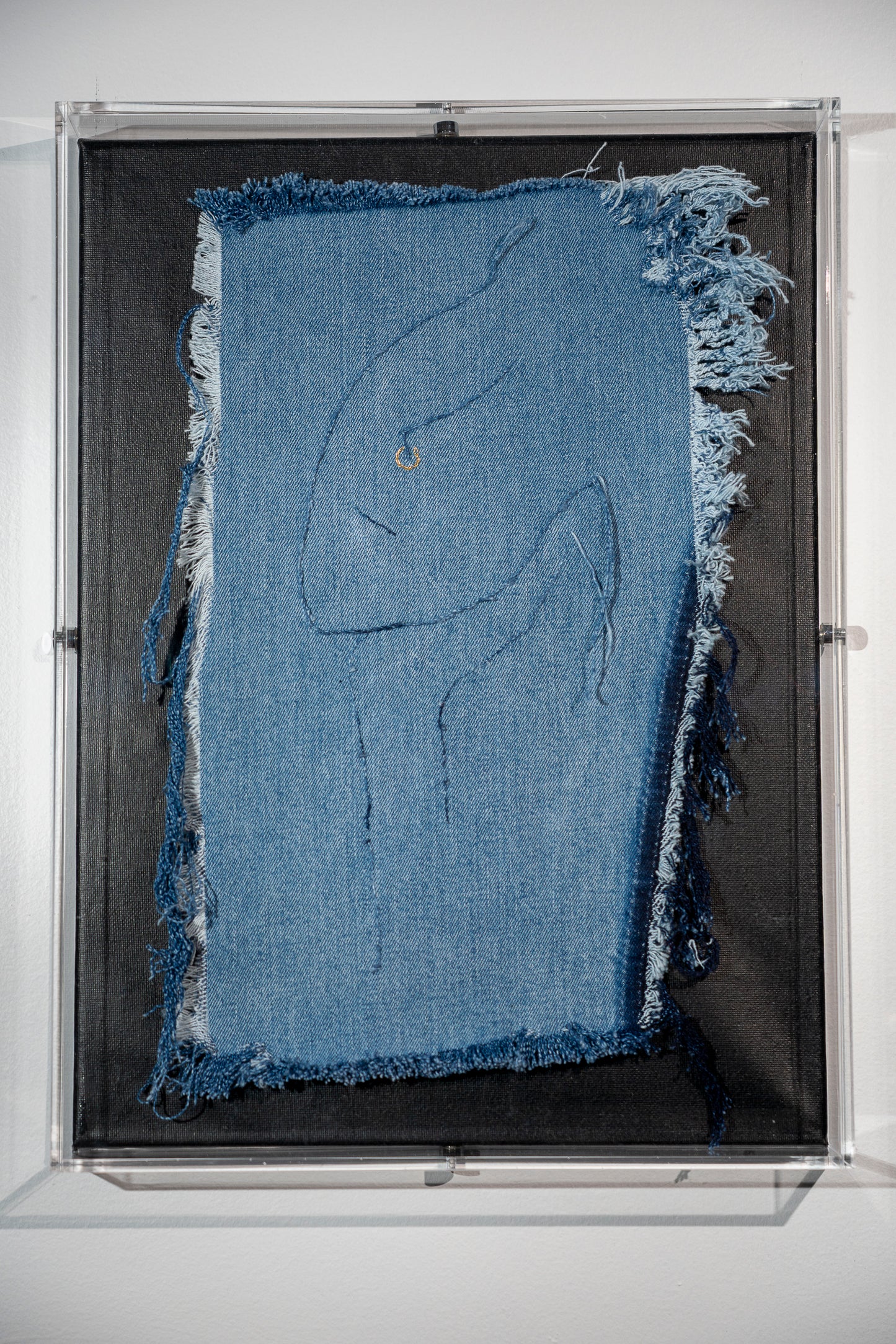 it is a piece of frayed denim with a very stylized suggestion of a female face resting on her hand in the style of the Dali statue. The image is created using the threads from the denim itself except for the pop of fun in a gold nose ring