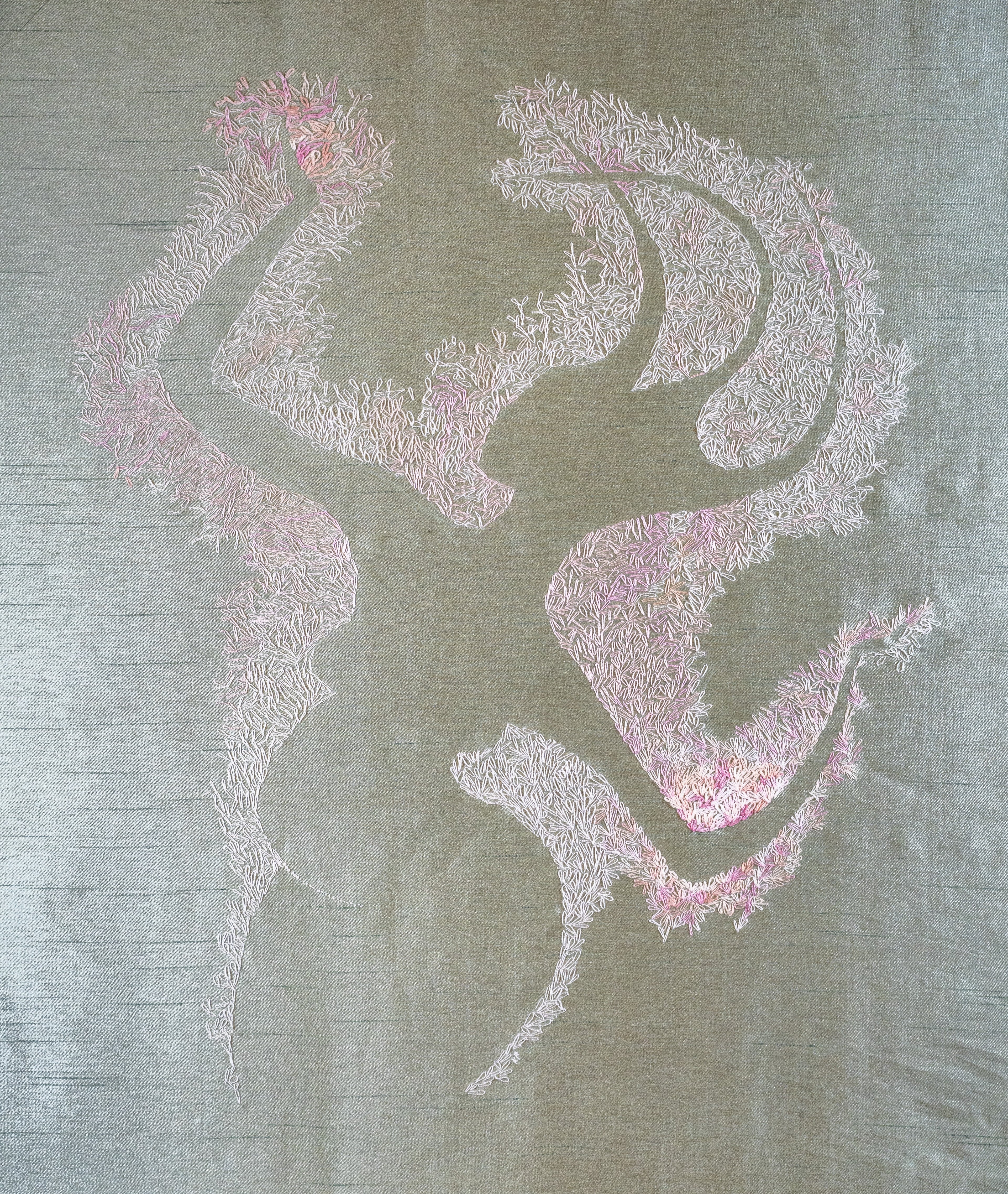 It is an abundance of peach blossoms creating the shape of a fertility goddess in the negative space. It is done in a variety of pink and peach threads on green raw silk.