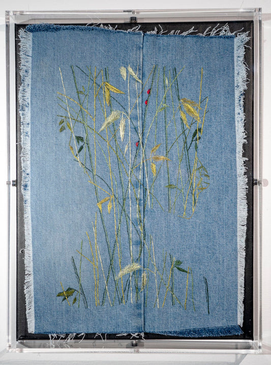On frayed blue denim, a face is revealed in the negative by seeing the outline made up of a growth of bamboo shoots dotted with three ladybugs, done in glossy threads.