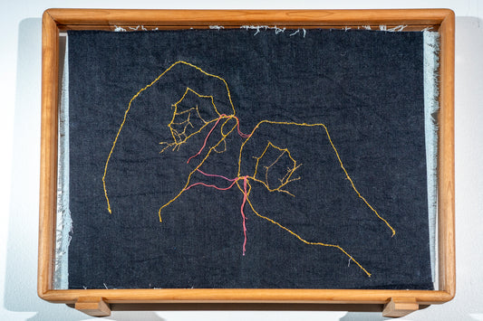 It is a double sided piece of denim with frayed edges, on each side is a pair of hands but on the dark side they are picking each other apart and on the light side they are sewing each other together with an actual needle embroidered into the piece. The hands are in gold thread but the threads being picked out are in shades of red.