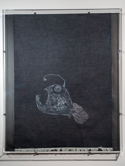 It is a large piece of dark denim with an angler fish embroidered in shades of grey in a contemporary embroidery style. She is inspired by the angler fish that was an internet sensation recently. Named it Hope. The top of the denim wraps into the frame so it is out of sight and the bottom is frayed.
