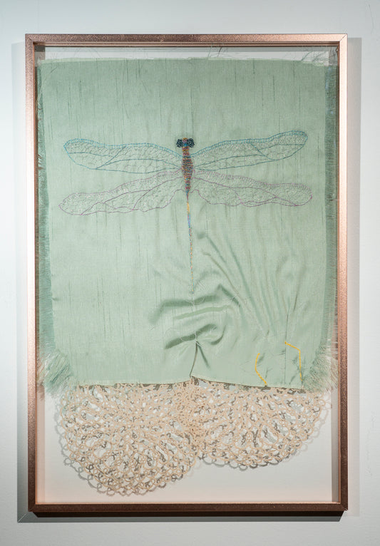 A dragonfly, done in iridescent thread, on raw green silk is escaping from the suggestion of a spider in a web. Vintage lace doilies peek out from below hinting at webs and insect eyes.