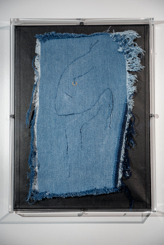 it is a piece of frayed denim with a very stylized suggestion of a female face resting on her hand in the style of the Dali statue. The image is created using the threads from the denim itself except for the pop of fun in a gold nose ring